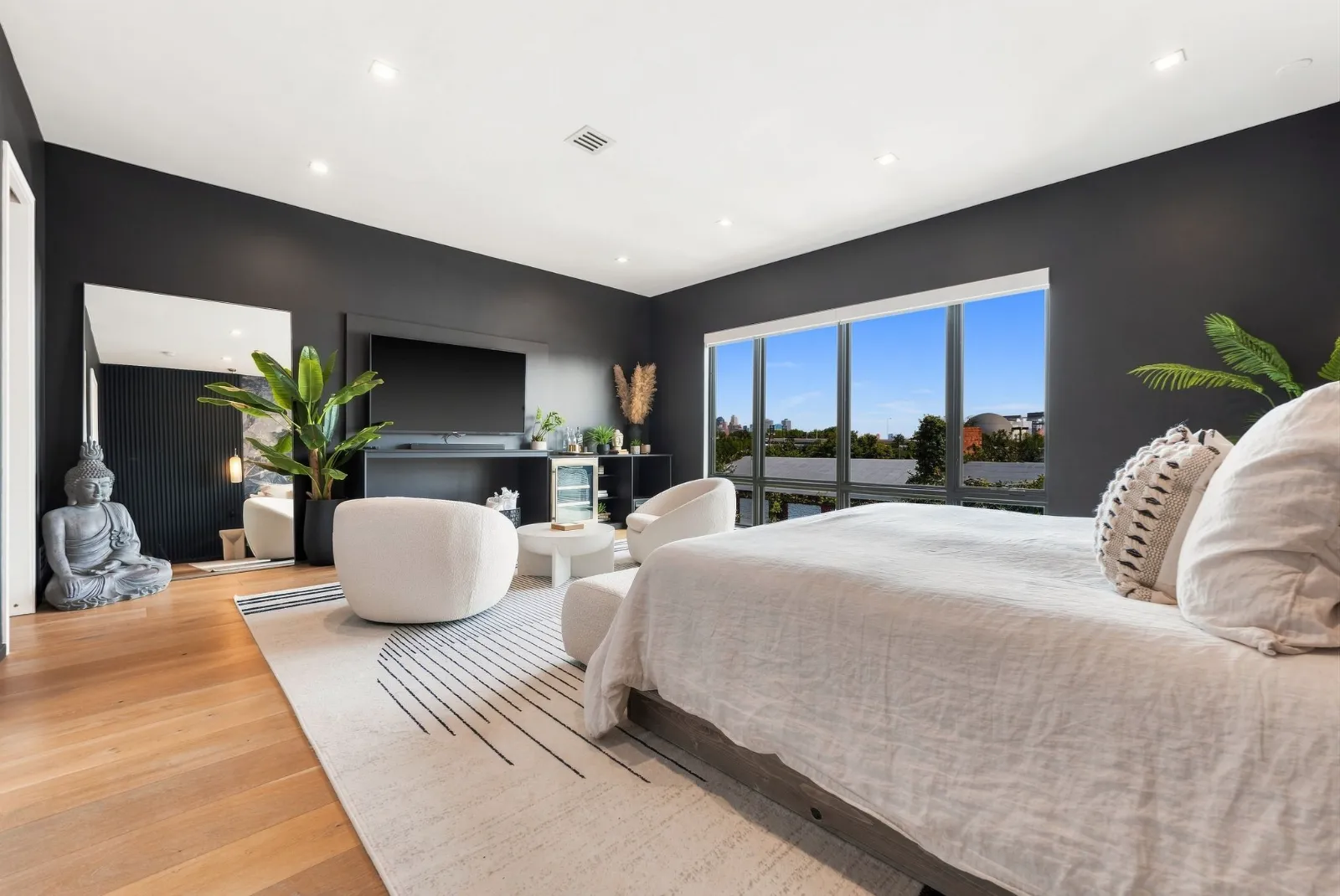 The primary bedroom with a wall of windows, dark accent wall and sculptural lounge chairs